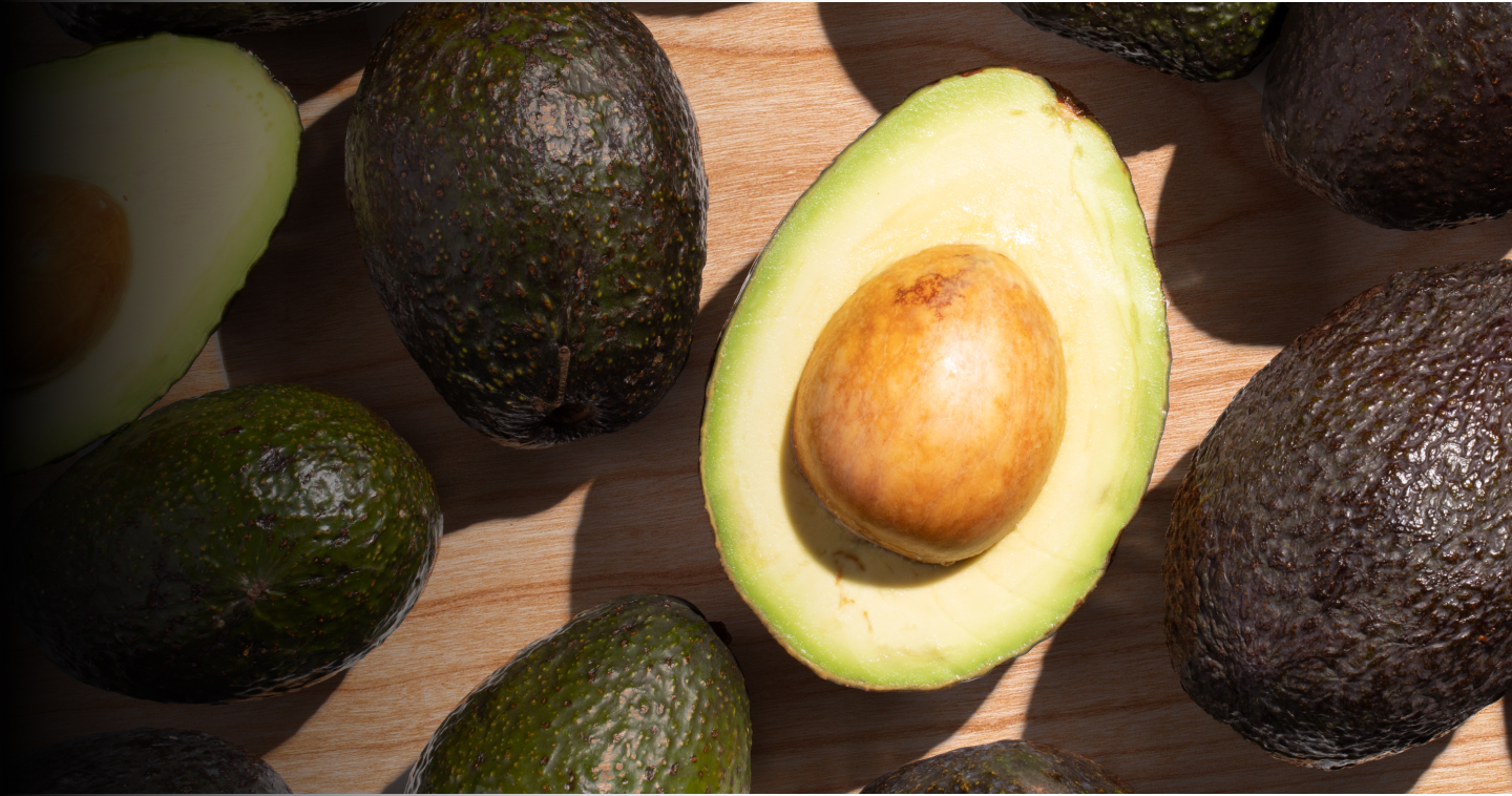 A wood cutting board of perfectly ripe Hass avocados with one cut in half exposing the pit.